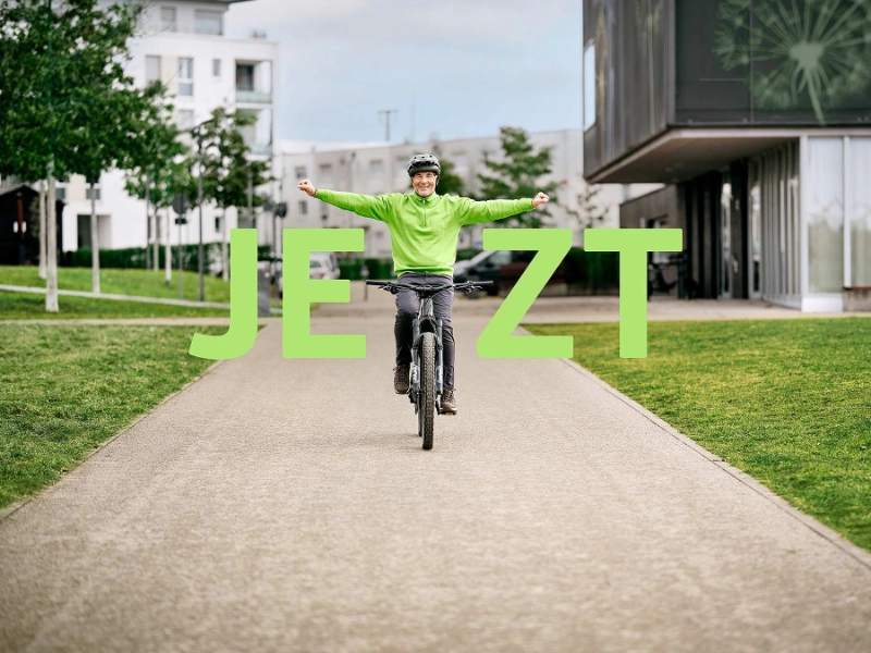 JobRadler fährt strahlend auf seinem Fahrrad mit gestreckten Armen mit Schriftzug "Jetzt" JobRadler fährt strahlend auf seinem Fahrrad mit gestreckten Armen mit Schriftzug "Jetzt"