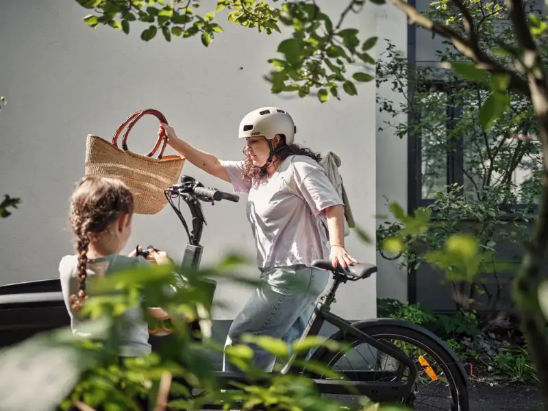 Eine Frau holt einen Korb aus dem Lastenrad, im Vordergrund schaut ein Kind zu