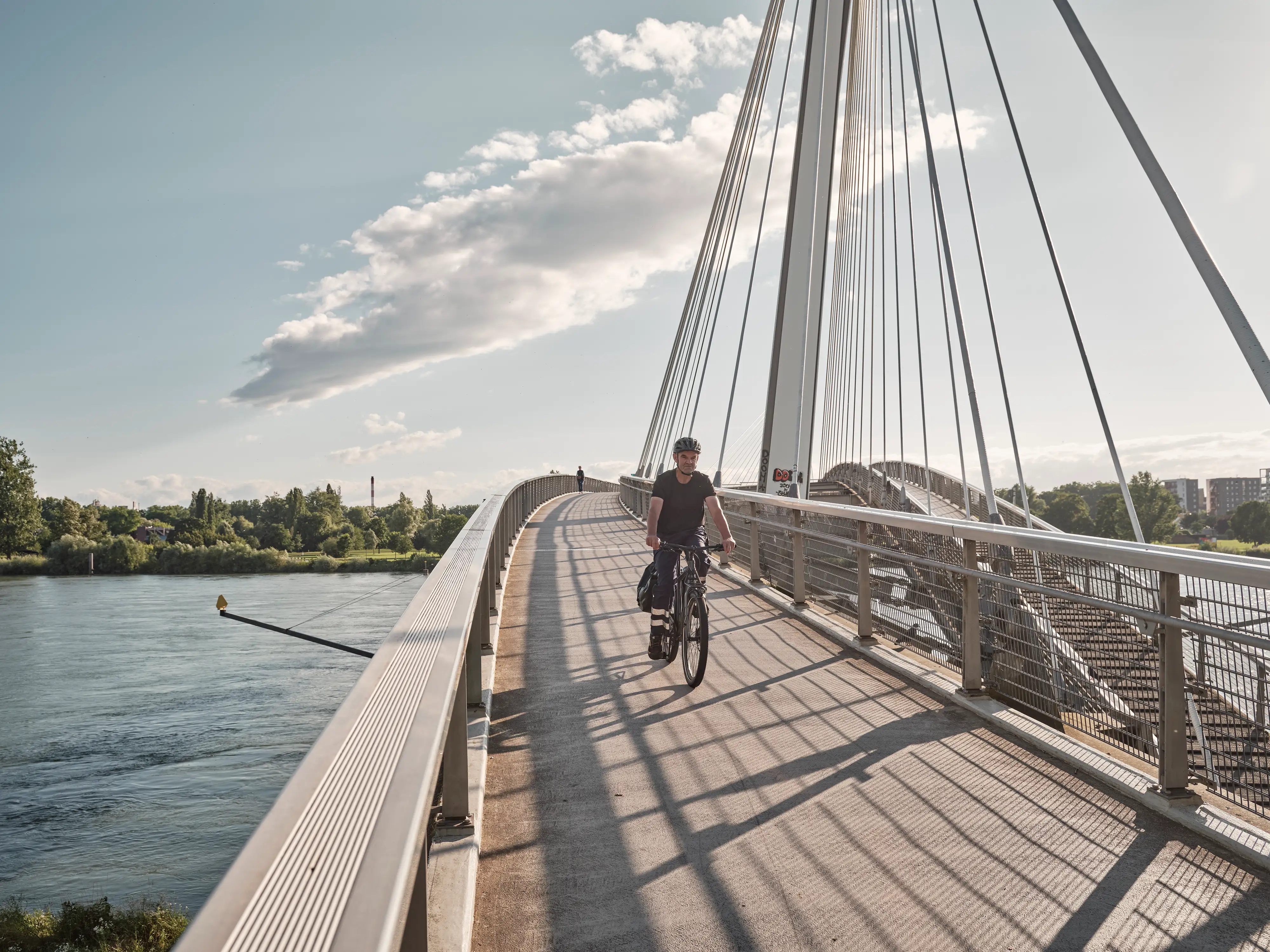 Radfahrer in Arbeitskleidung auf Fahrradbrücke über Fluss