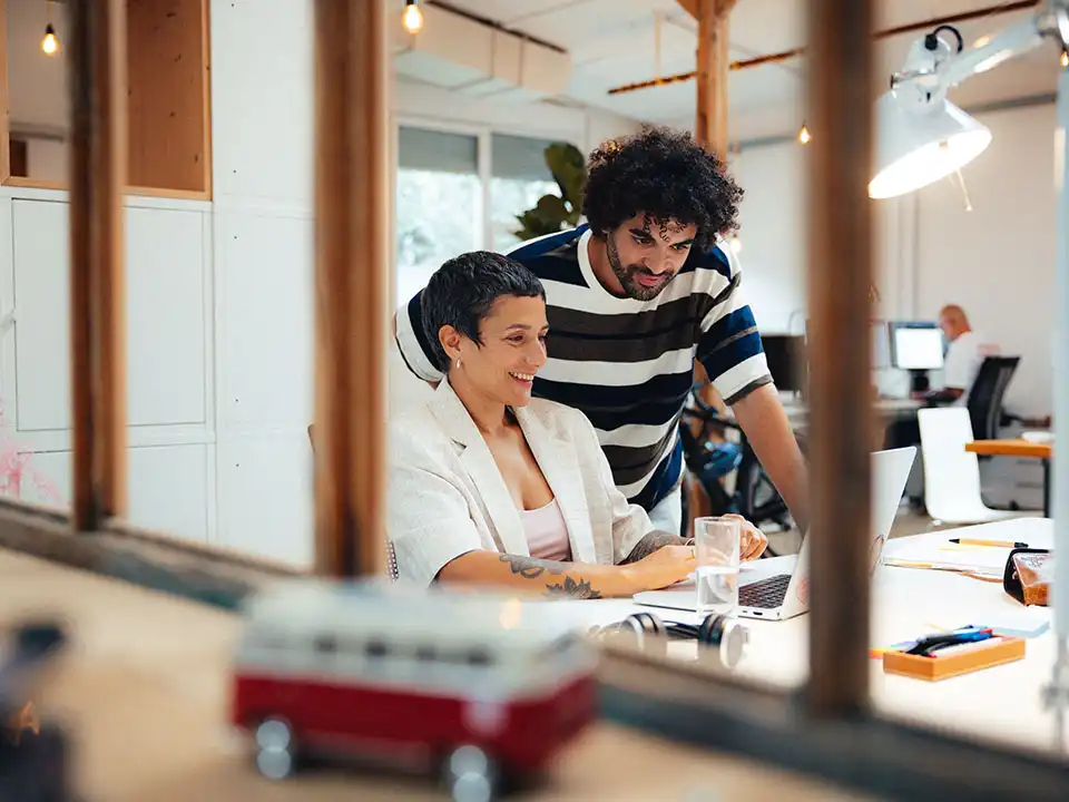 Mitarbeitende schauen begeistert zusammen auf Laptop im Büro