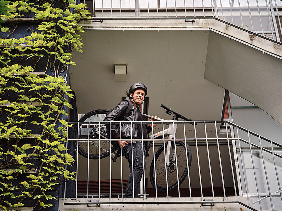 JobRadler trägt Fahrrad die Treppe herunter und lacht in Kamera