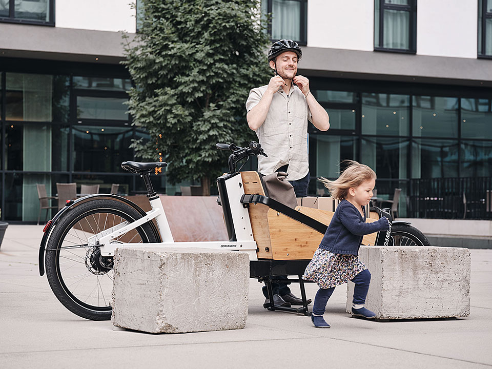 Lastenradler mit weißem Lastenrad parkt in der Stadt, sein Kind läuft los