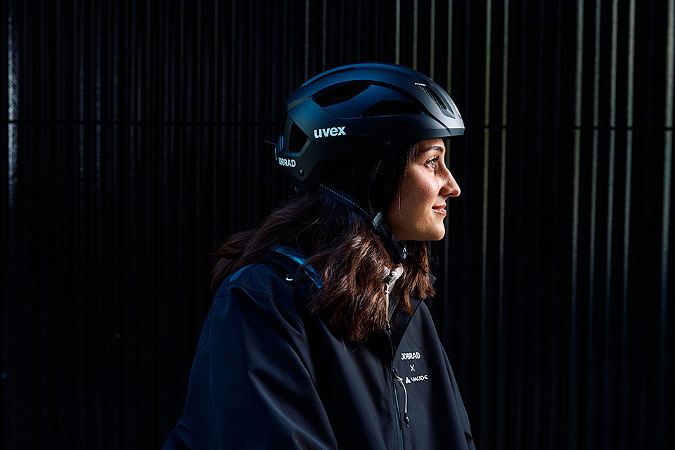 GENVELO visual eine Frau mit Fahrradhelm und Jacke im Profil vor dunkler Wand