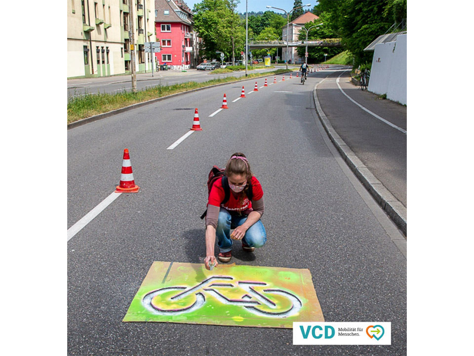 Vertreterin des Verkehrsclub Deutschland sprüht Fahrrad auf Straße in Freiburg
